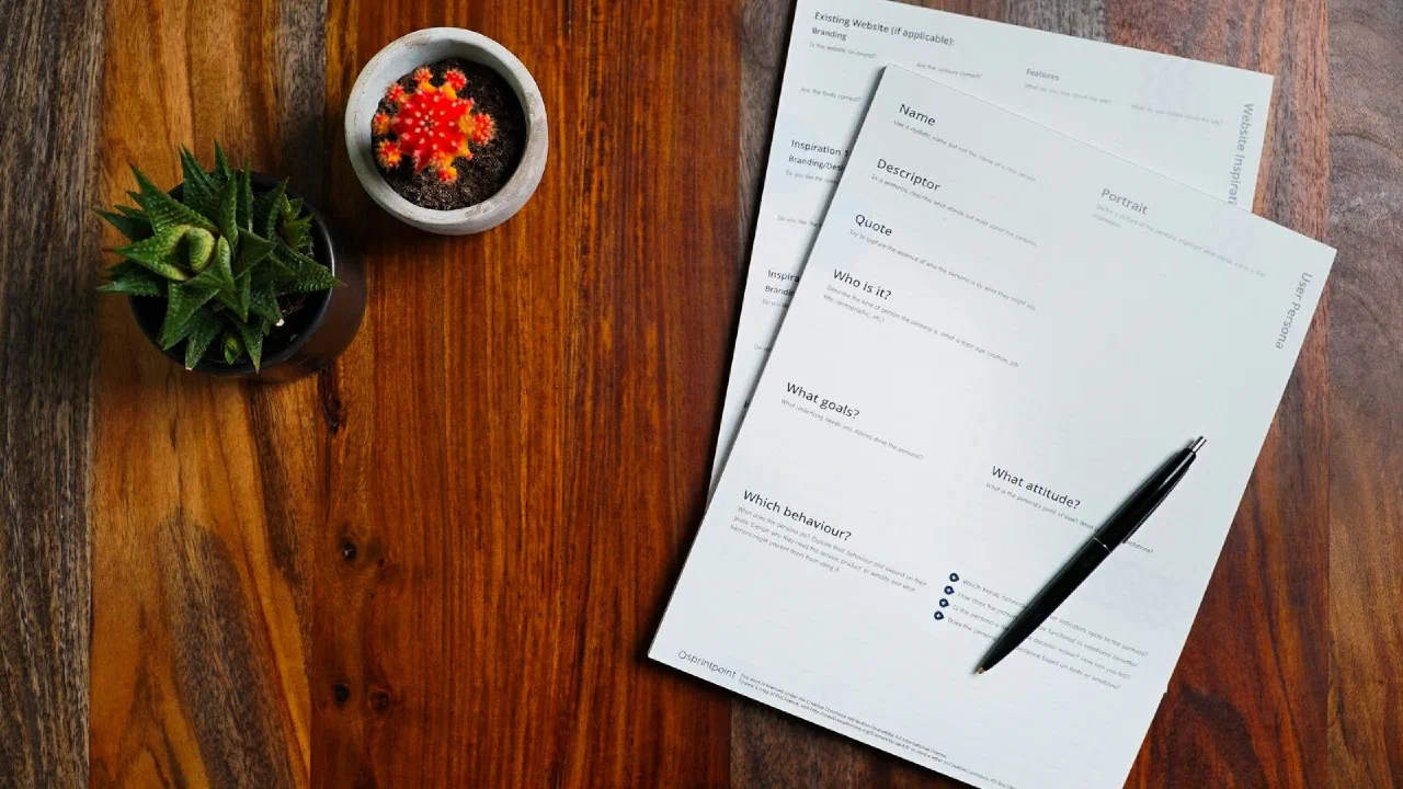 Printed papers and a pen spread across a wooden table
