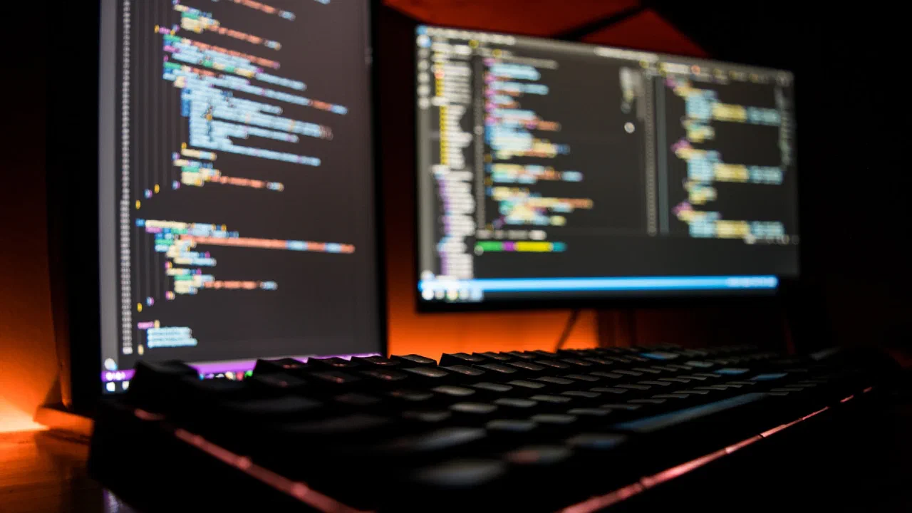 A dark keyboard in front of a screen of code