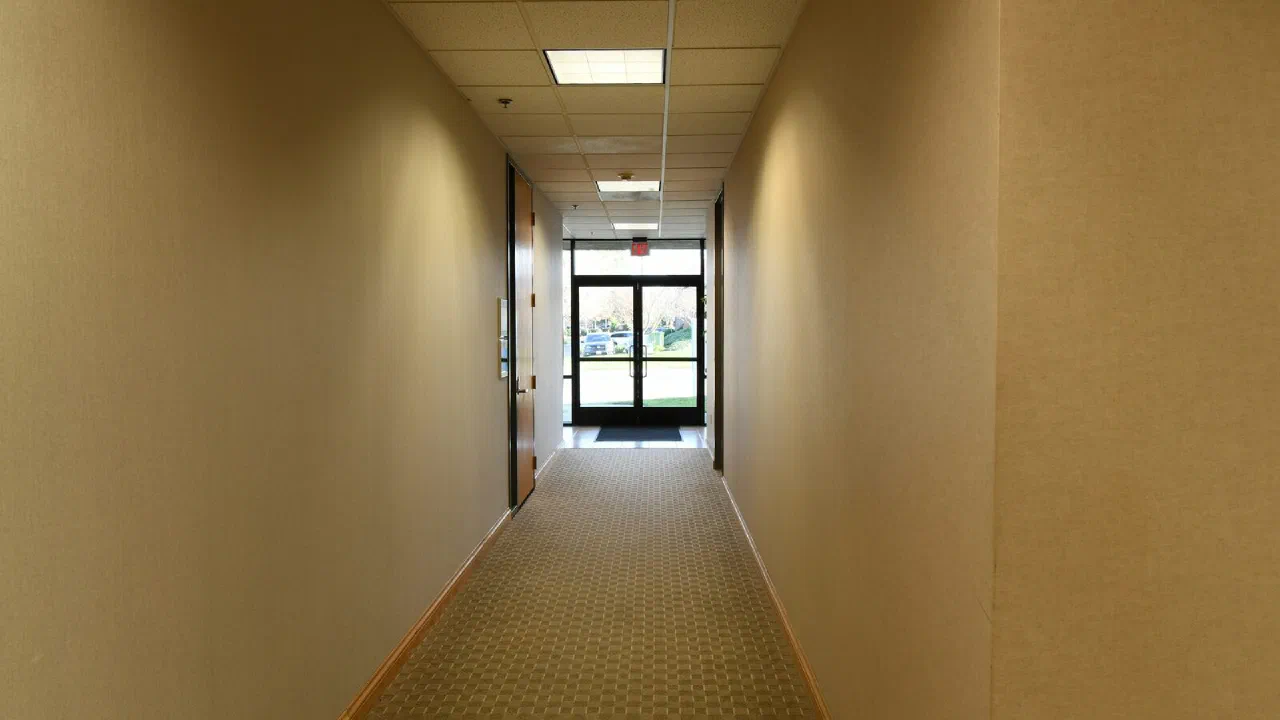 A long, empty corridor with beige walls and a door at the far end
