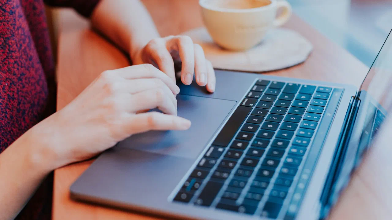 An open laptop on a desk with someone working at it